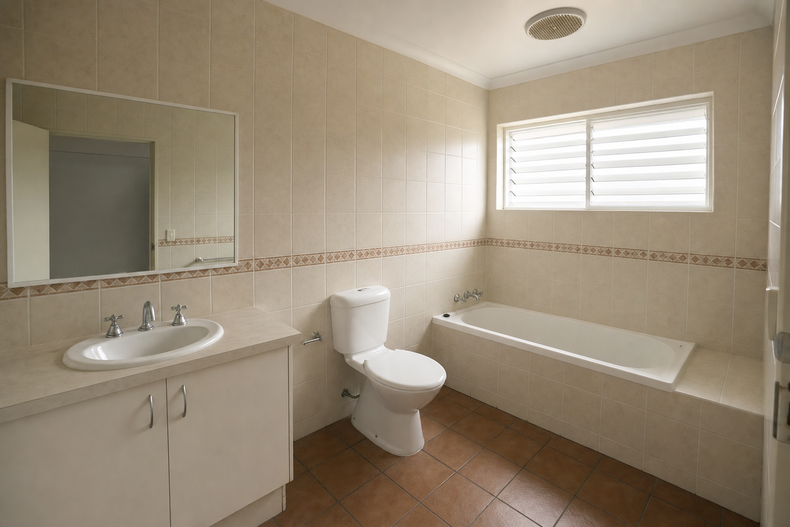 Dated 1990s bathroom with cream wall tiles, terracotta floor and laminate vanity, before renovation
