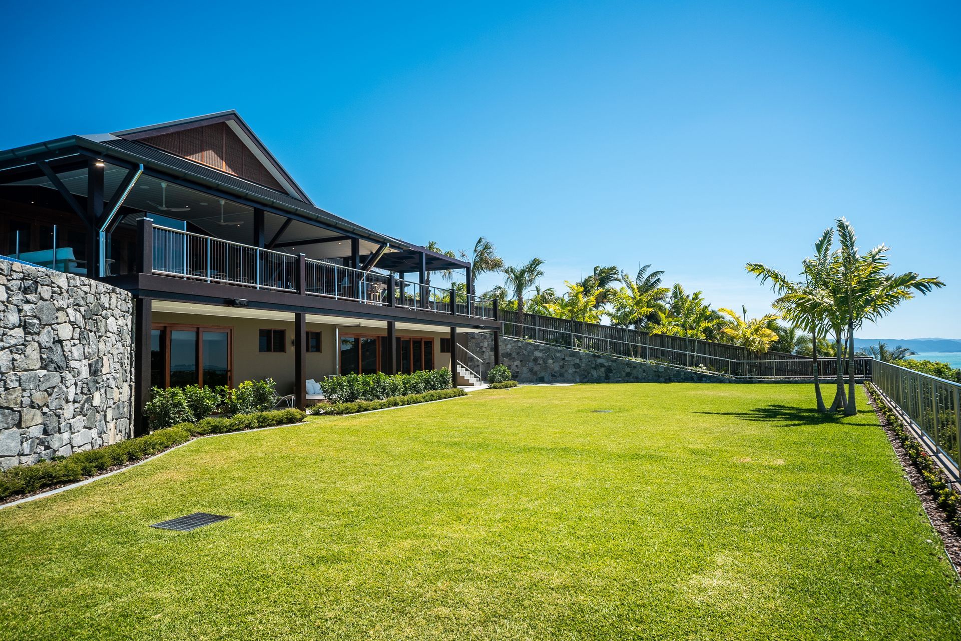 Element Hill private residence, Hamilton Island — exterior with pitched steel roof, timber-lined eaves, stone walling and elevated deck