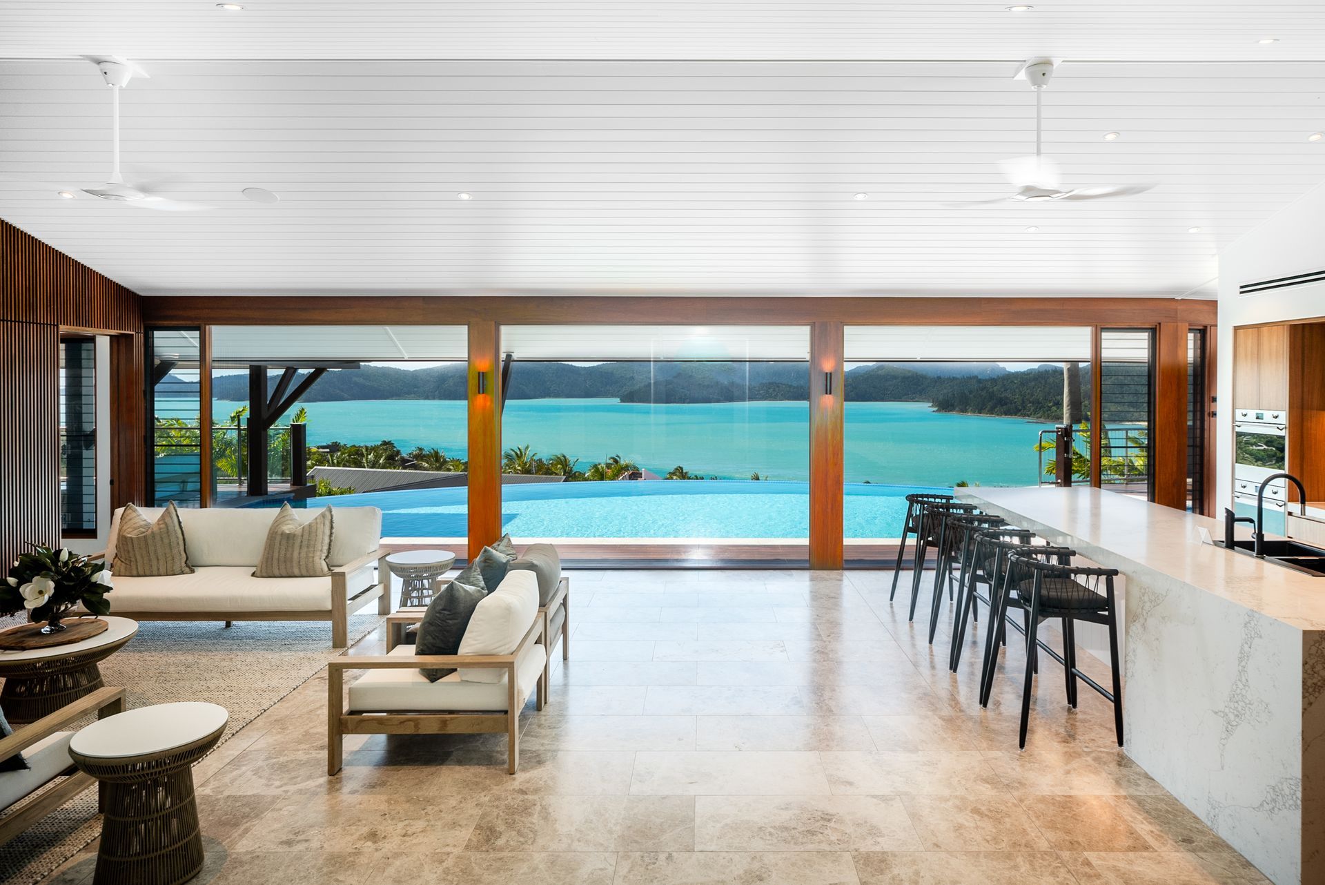 Element Hill interior — open-plan living and kitchen with timber-framed sliding doors opening to an infinity pool over the Whitsundays