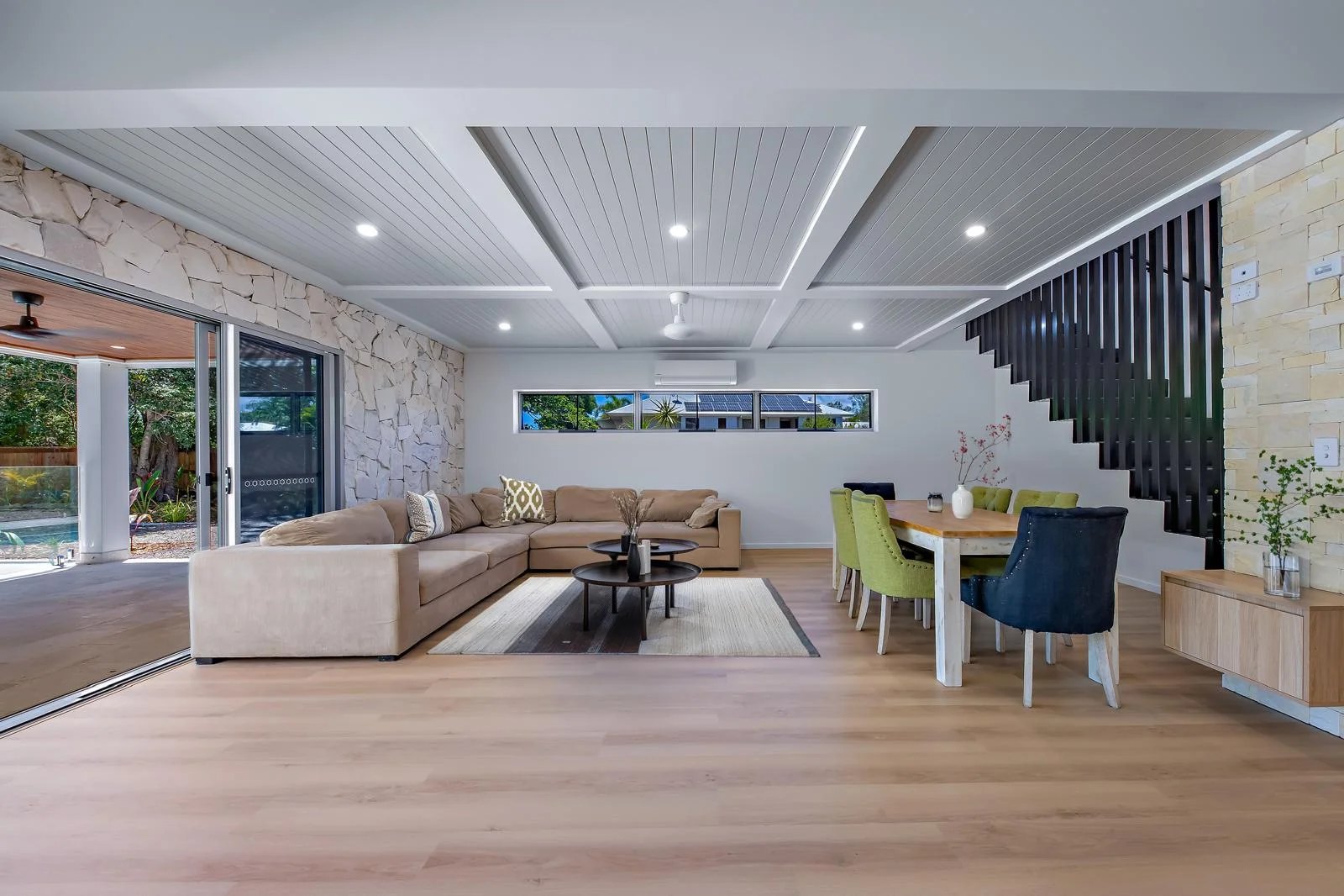 Private Hideaway Bay residence living and dining — coffered timber ceiling above the staircase, feature stone wall and continuous oak flooring