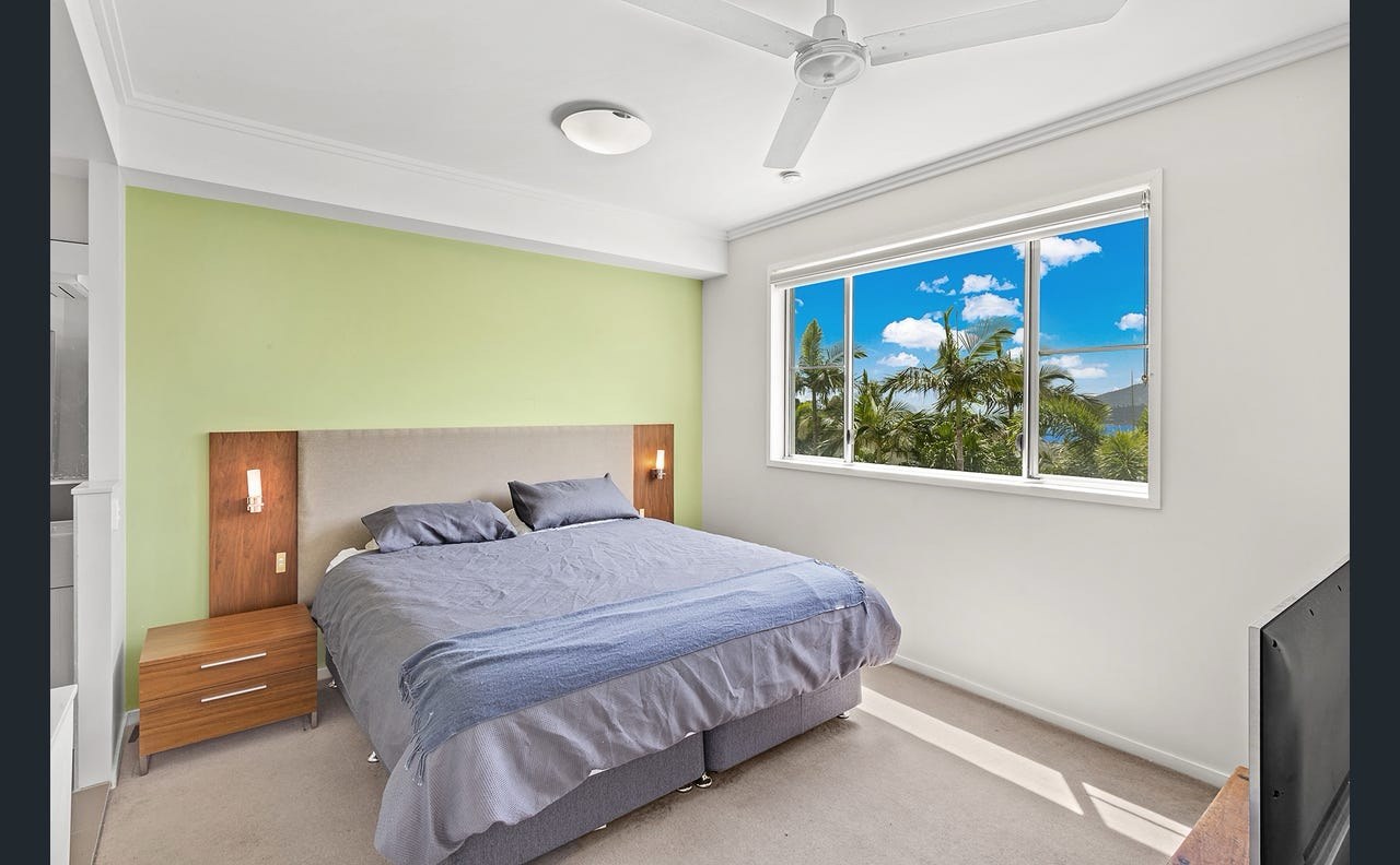 Master bedroom at Nalani Airlie Beach before renovation — dated pale-green feature wall behind a plain walnut headboard