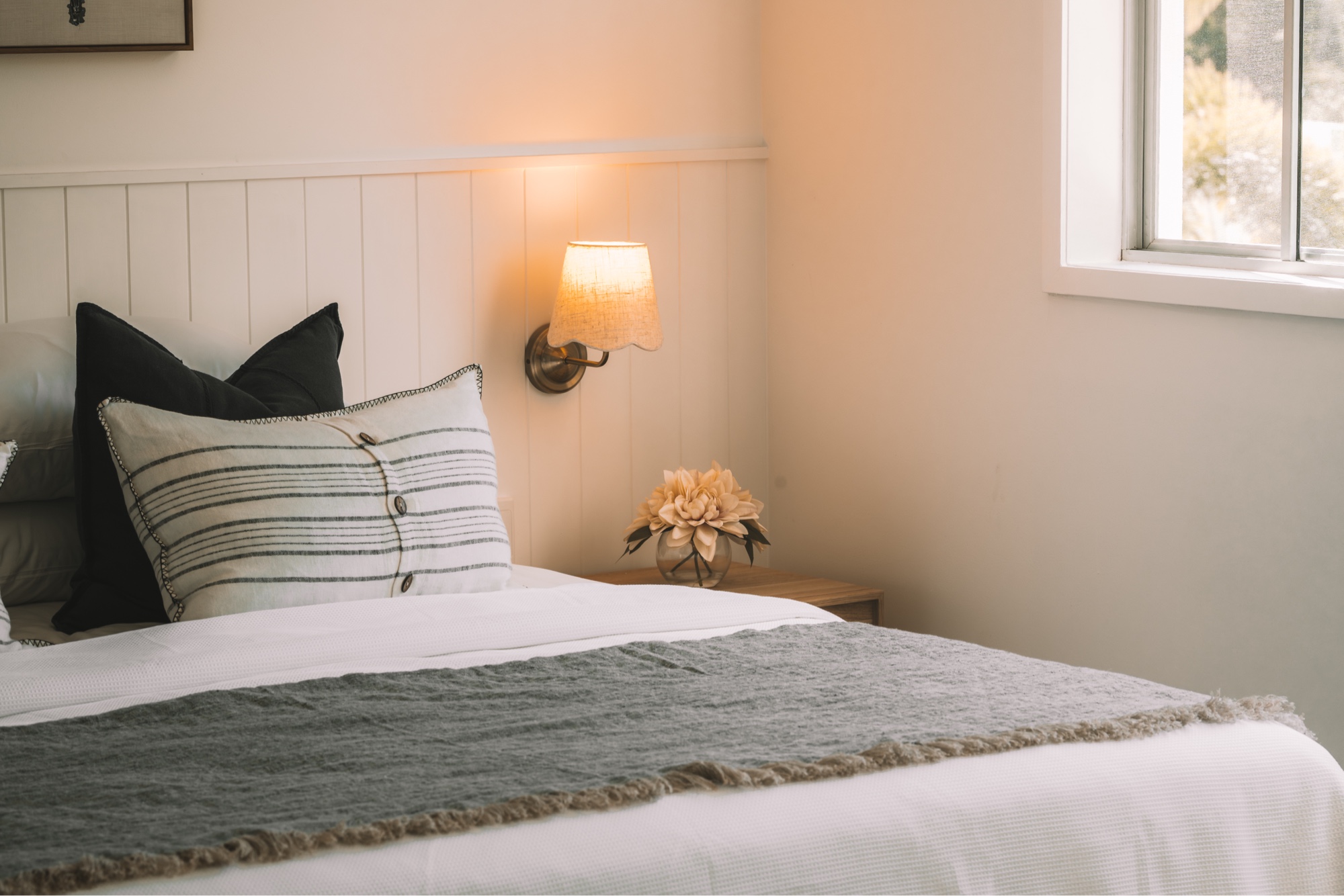 Master bedroom at Nalani Airlie Beach after renovation — white vertical VJ feature wall with brass wall sconce, styled bed linen and warm lamp light
